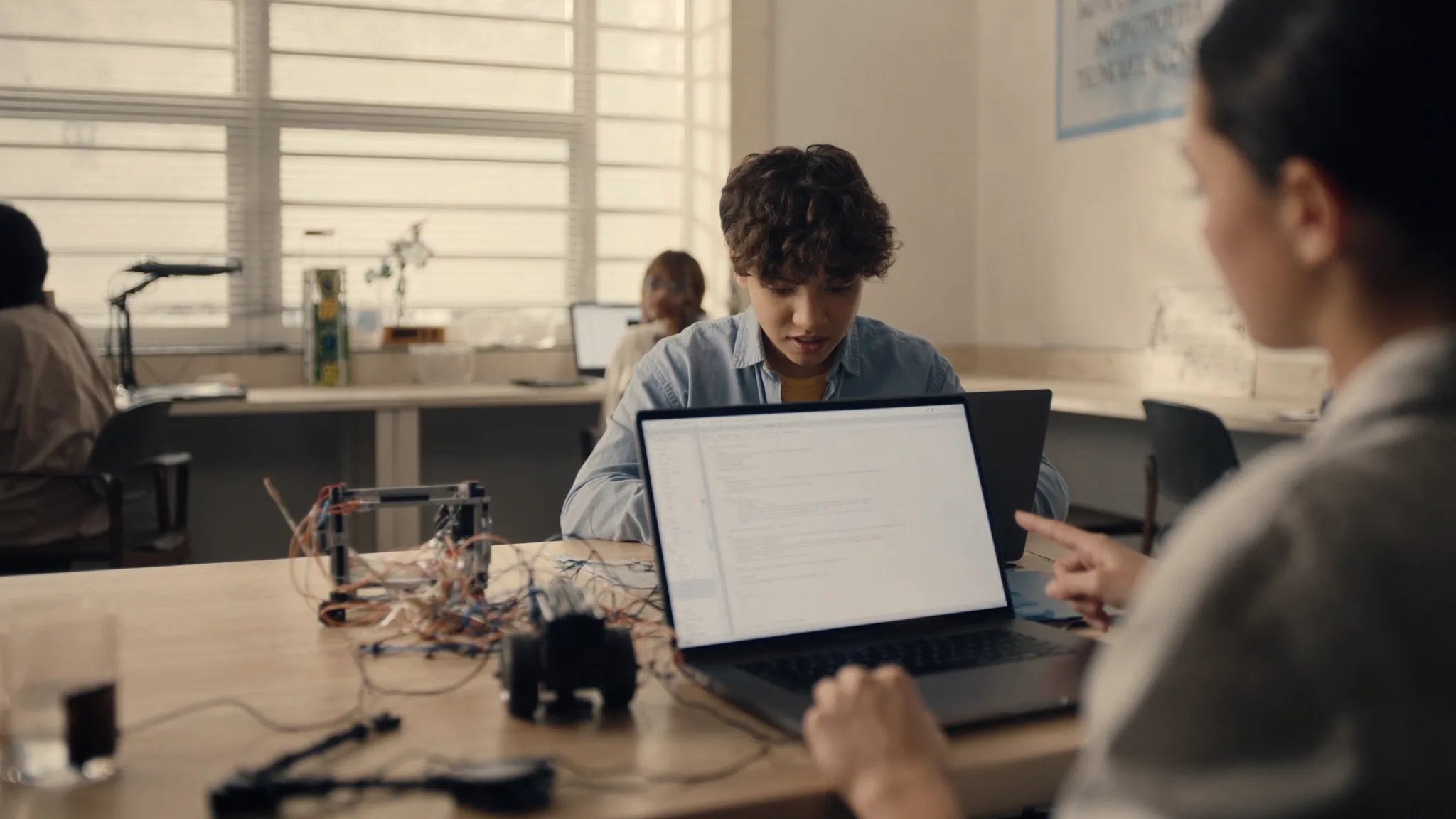 Teen working on a laptop beside a breadboard and wired electronics at a lab table