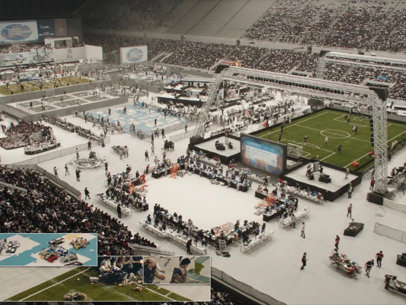 Aerial view of a packed arena hosting several robotics competition fields and pit areas