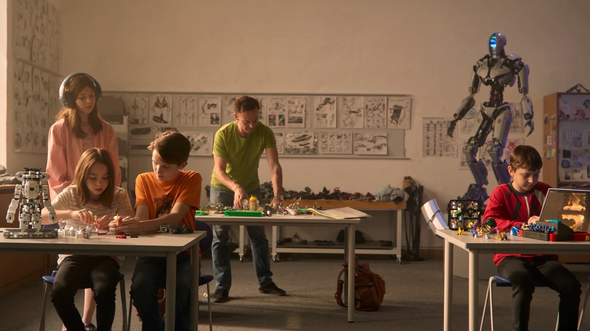 Children in headphones building small robots at tables with a tall humanoid robot in the corner