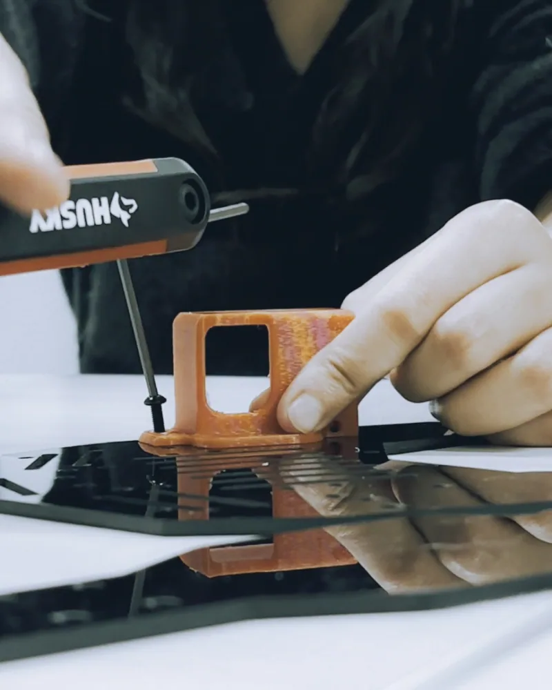 Close-up of hands using a hex screwdriver on an orange 3D-printed bracket