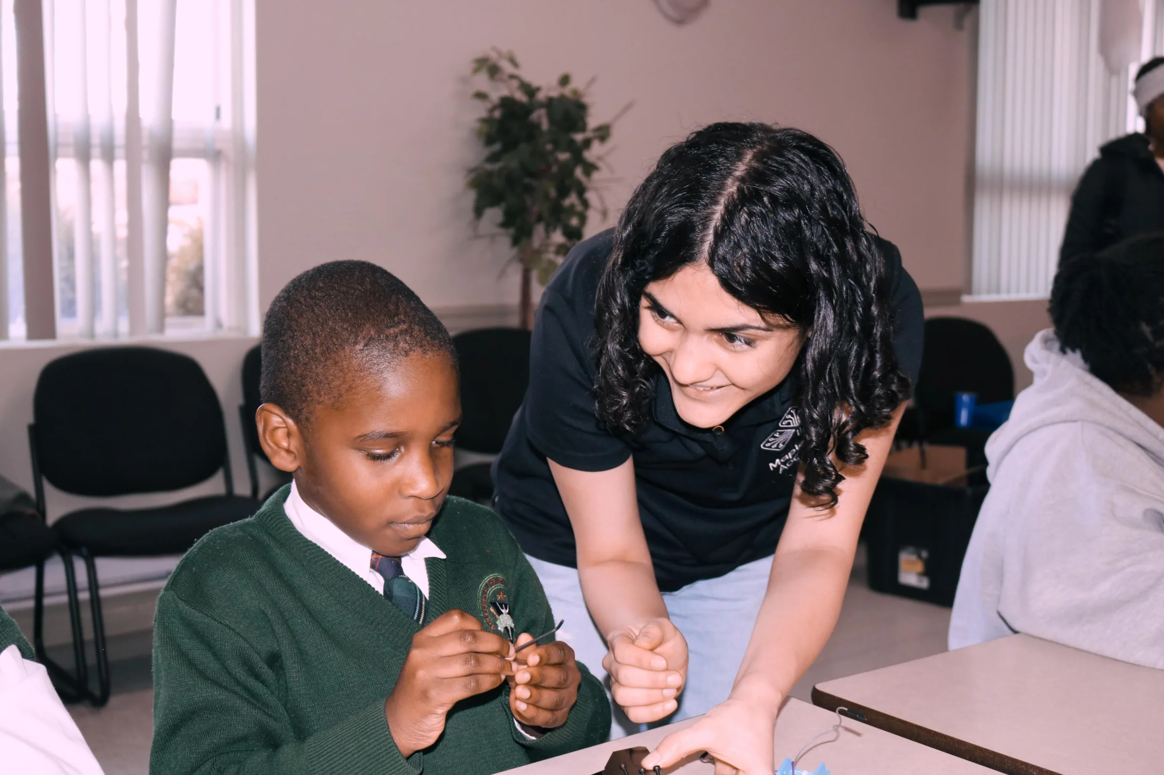 Instructor leaning in to help a boy in a school uniform with a small component