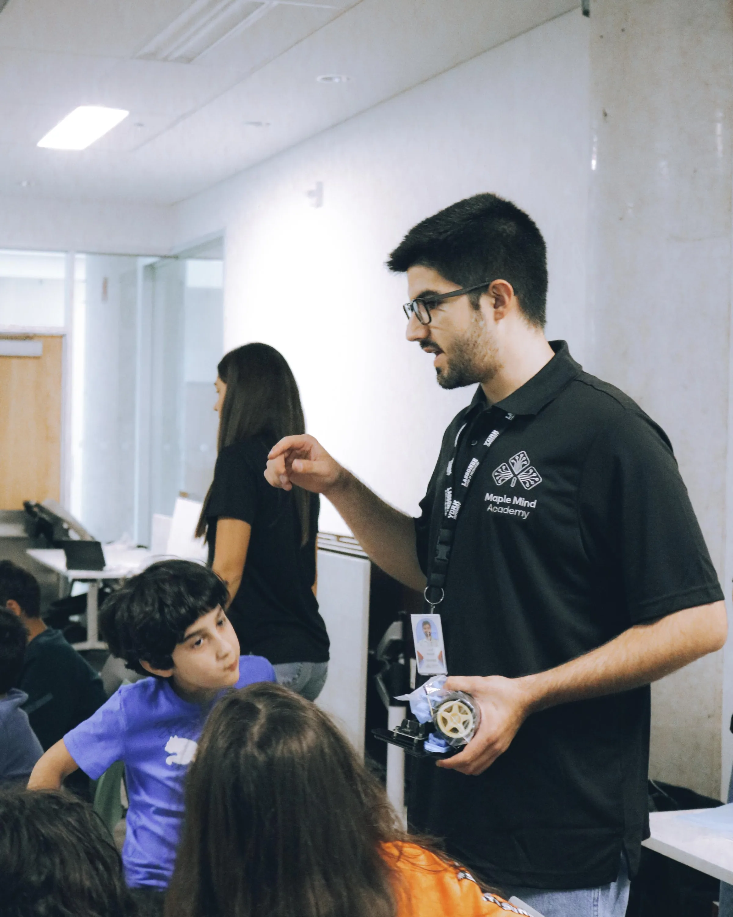Instructor holding a robot wheel assembly while explaining it to seated students