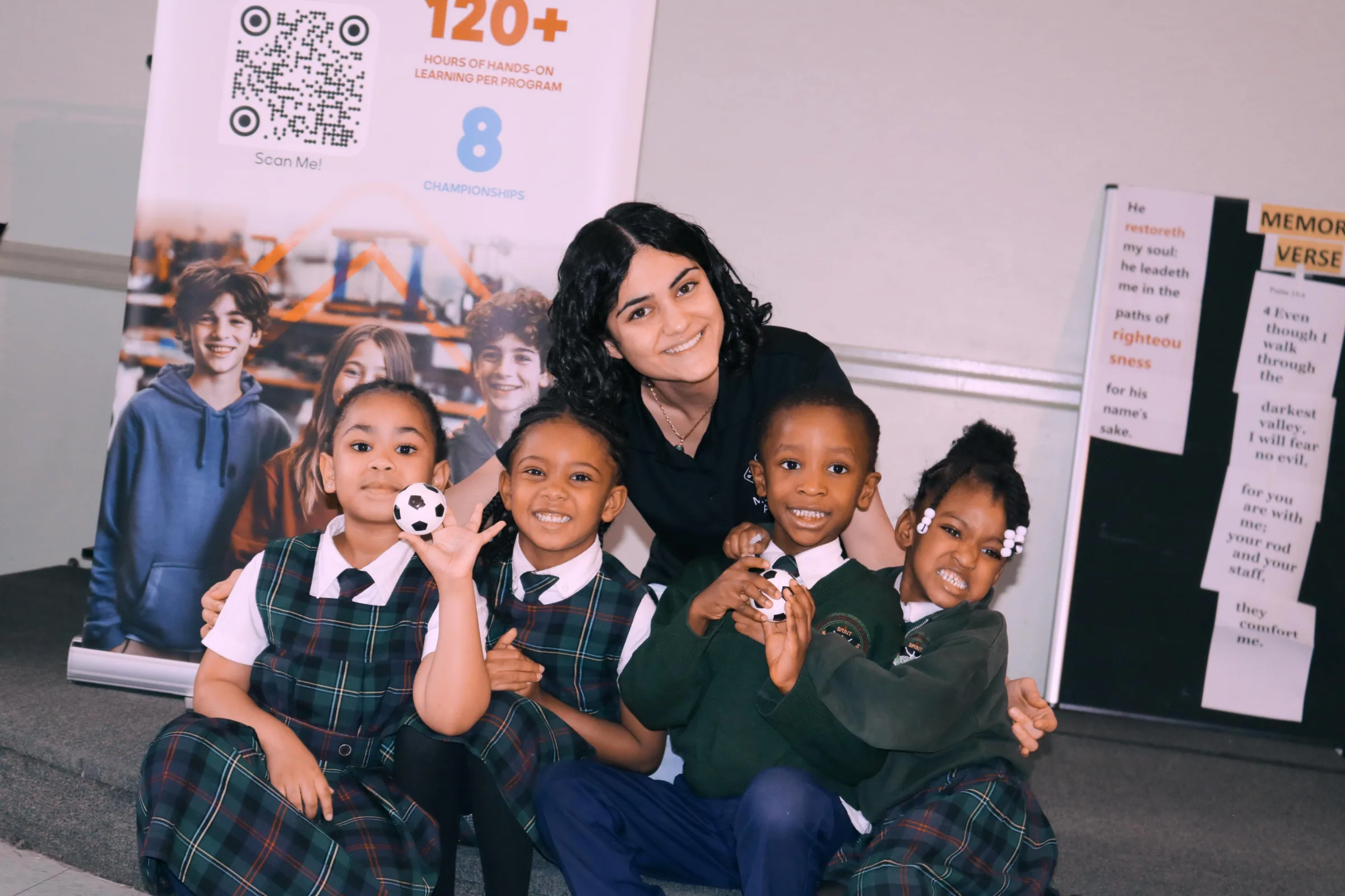 Smiling instructor crouching with four uniformed children in front of a program banner