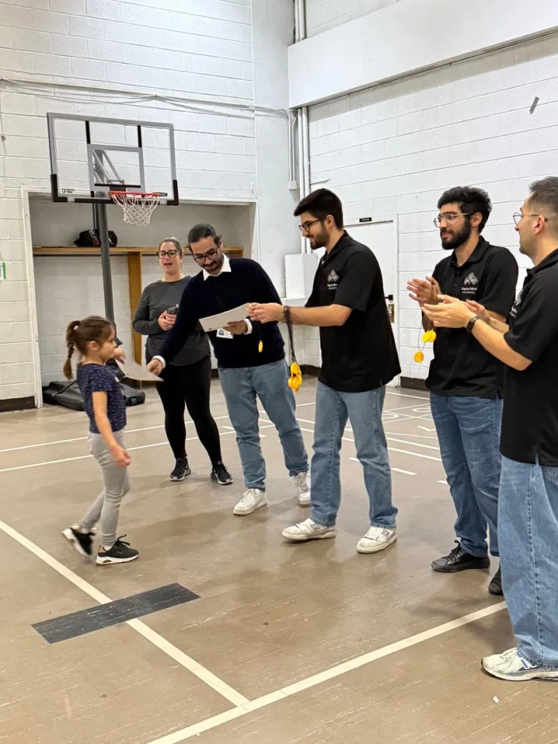 Instructors applauding as a young girl receives a certificate in a school gymnasium