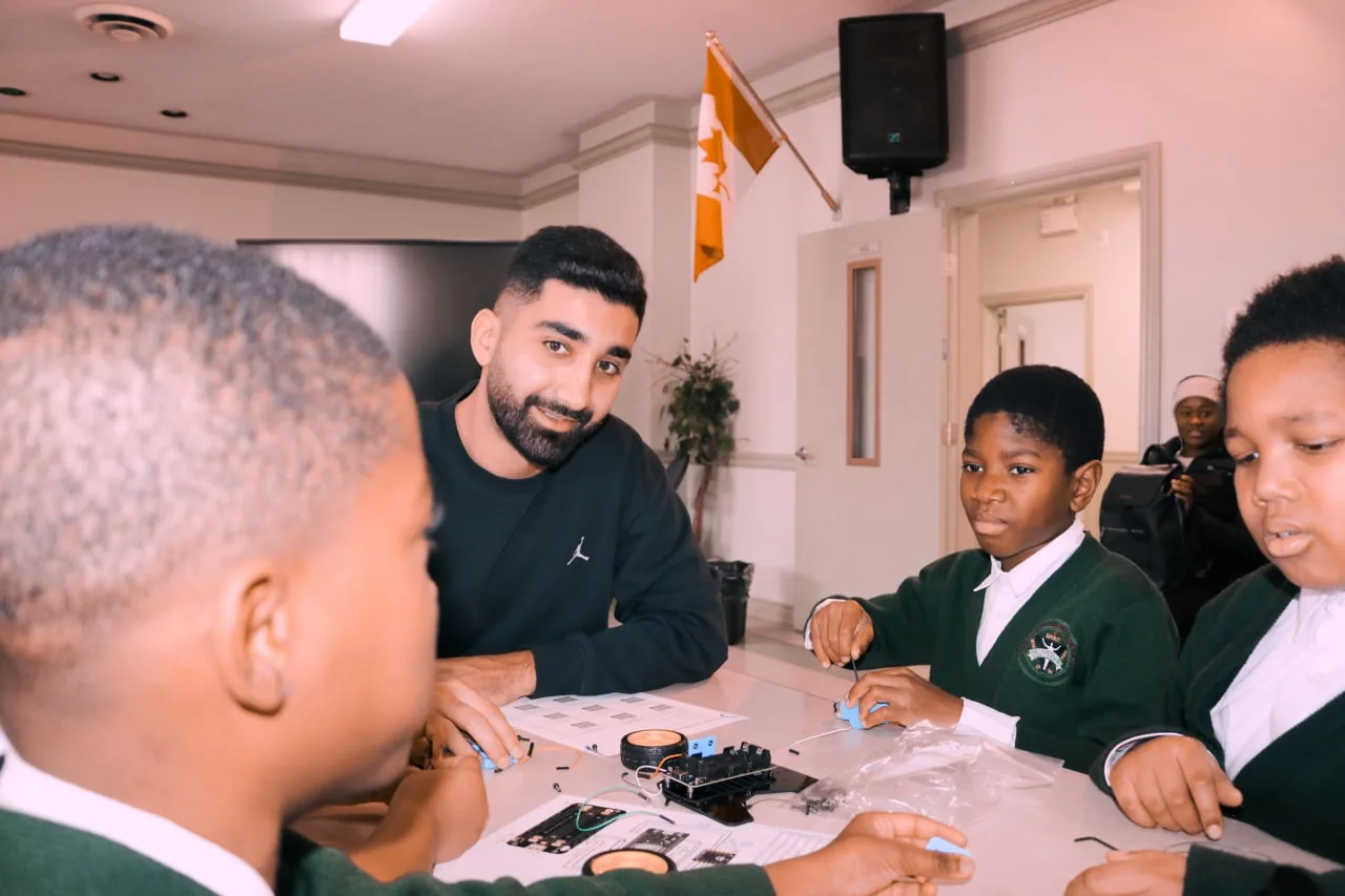 Instructor smiling beside children in school uniforms assembling small electronic kits at a table