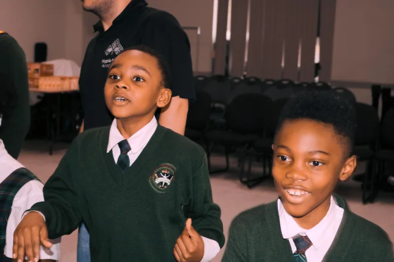 Two boys in school uniforms smiling and reacting excitedly beside an instructor