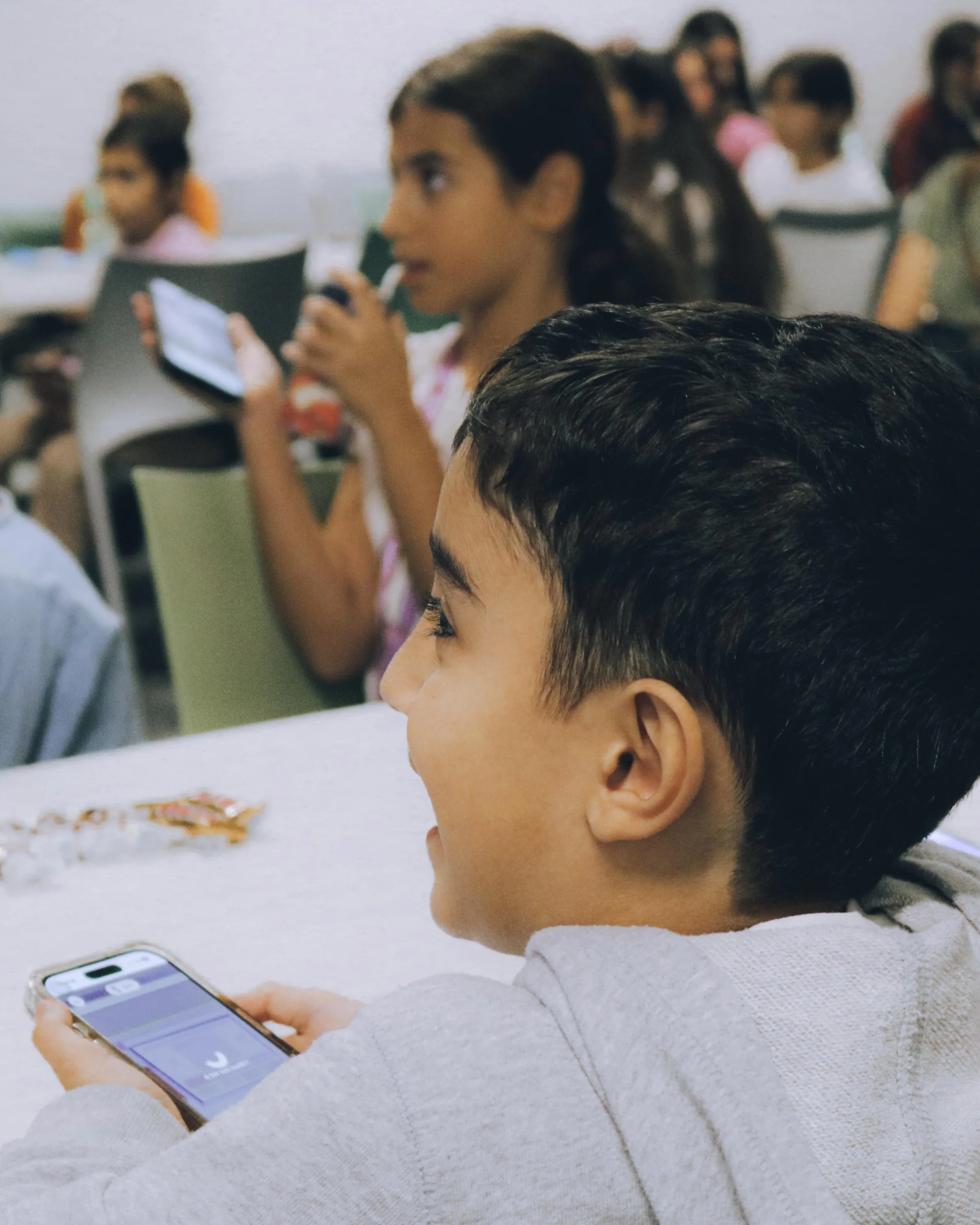 Smiling boy holding a phone controller during a busy classroom session