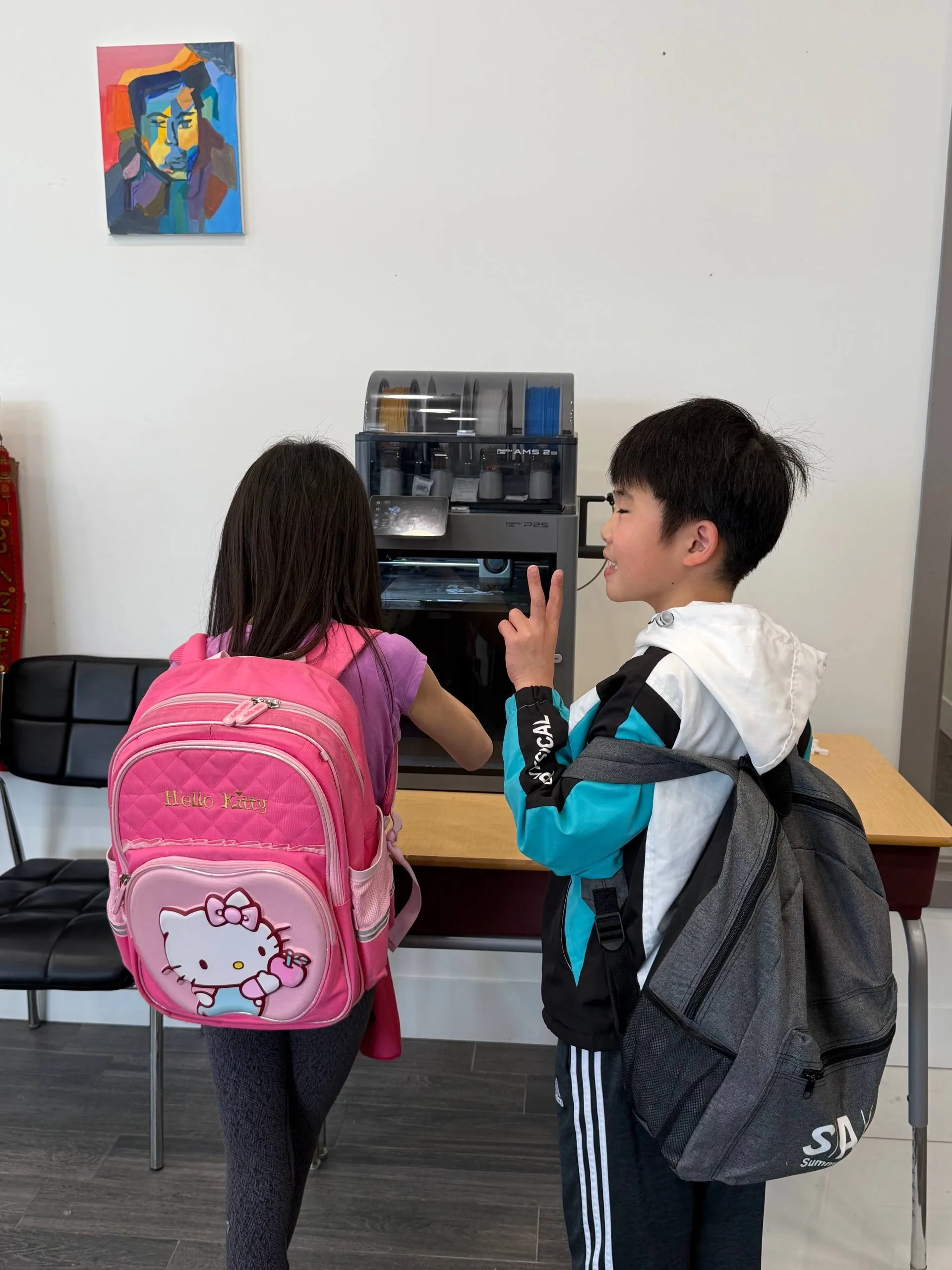 Two children with backpacks peering into an enclosed 3D printer, one making a peace sign
