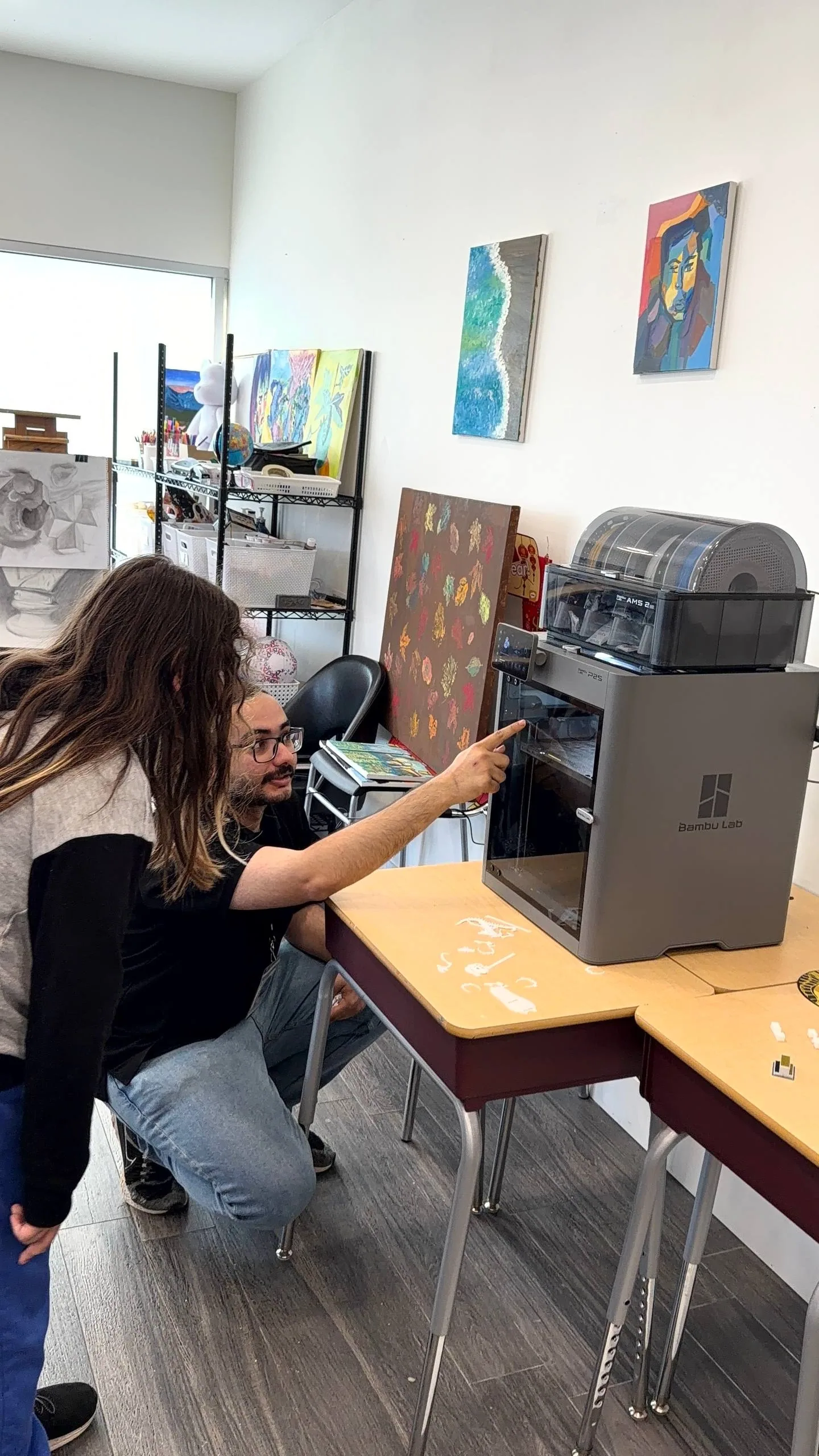 Instructor crouching to point out a 3D printer's controls to a girl