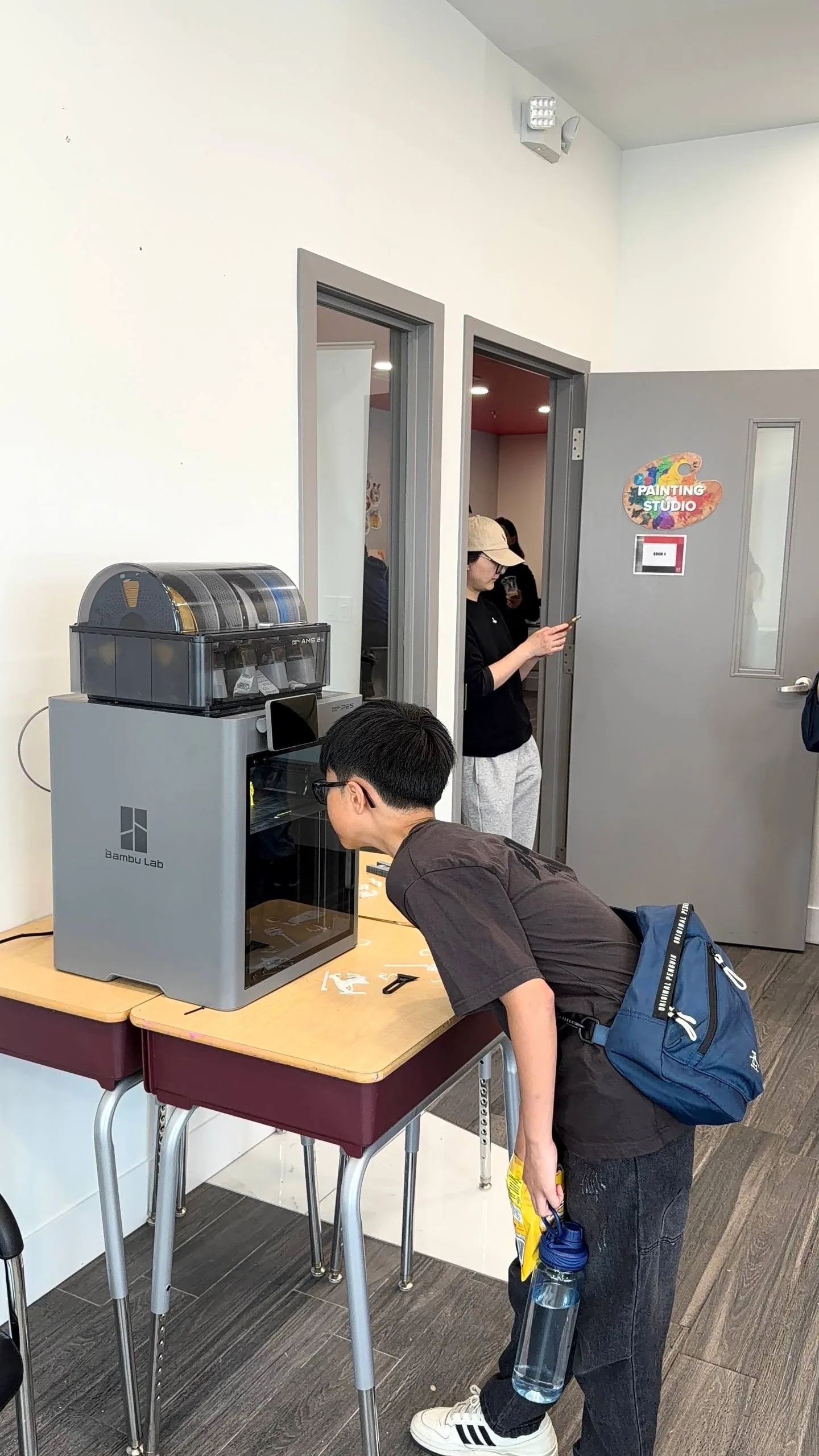 Boy with a backpack leaning in to look inside an enclosed 3D printer