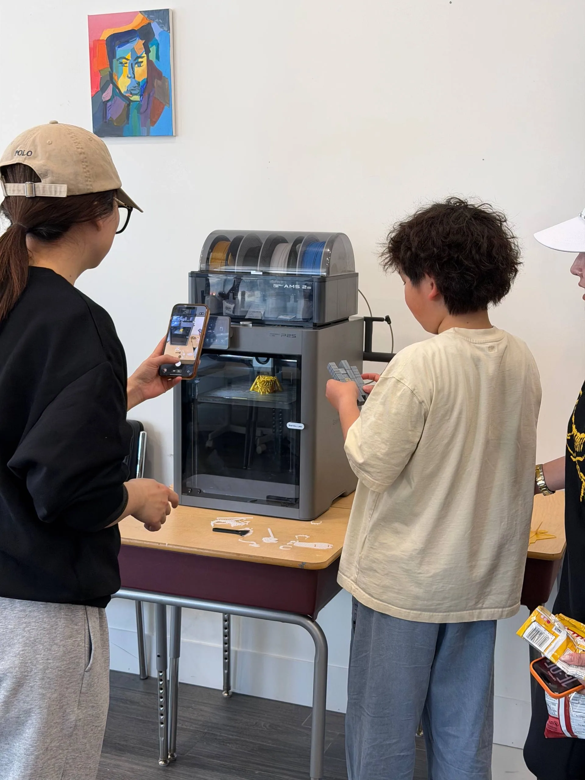 Teen photographing a 3D print in progress while another examines the printer