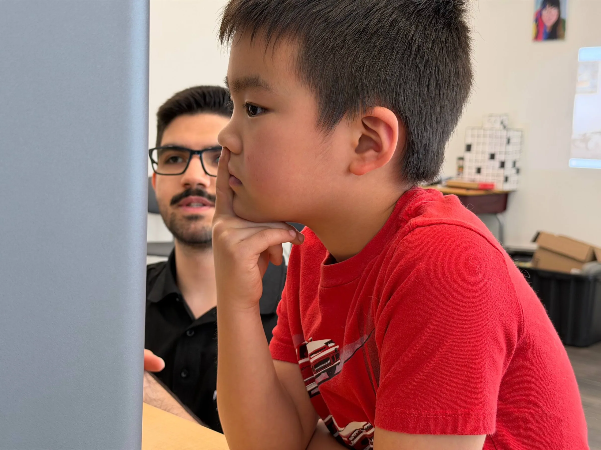 Boy resting his chin on his hand and listening thoughtfully as an instructor looks on